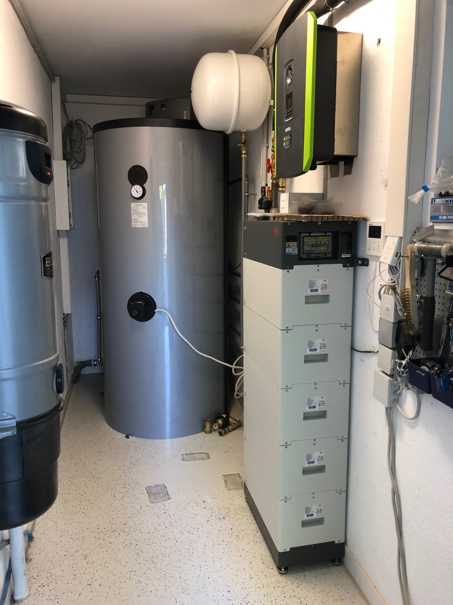 Batteriespeicher und Wechselrichter neben Warmwasserspeichern in einem Technikraum